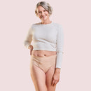 Frau trägt Periodenunterwäsche Inkontinenz-Panty-Strong in Nude mit grauem Oberteil und lacht.