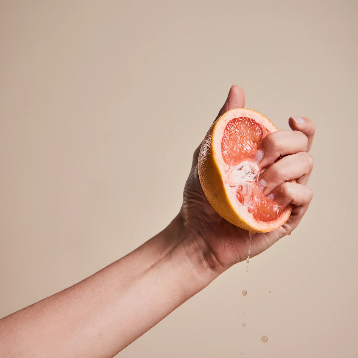 Hand drückt eine halbe Grapefruit aus