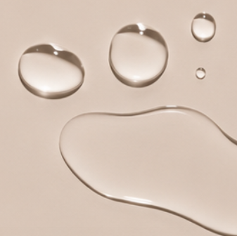 Clear drops of the Dry Touch Body Oil from the Touch Me Duo on a beige background, juno&me