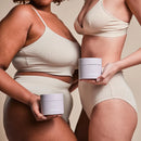 Frauen stehen einander zugewandt, halten 2in1-AHA-Body-Scrub in den Händen.