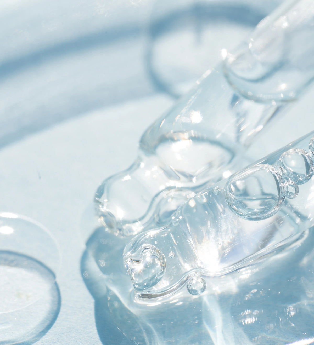 Tropfende Pipette gibt klare Flüssigkeit mit Luftblasen ab, blauer Hintergrund.
