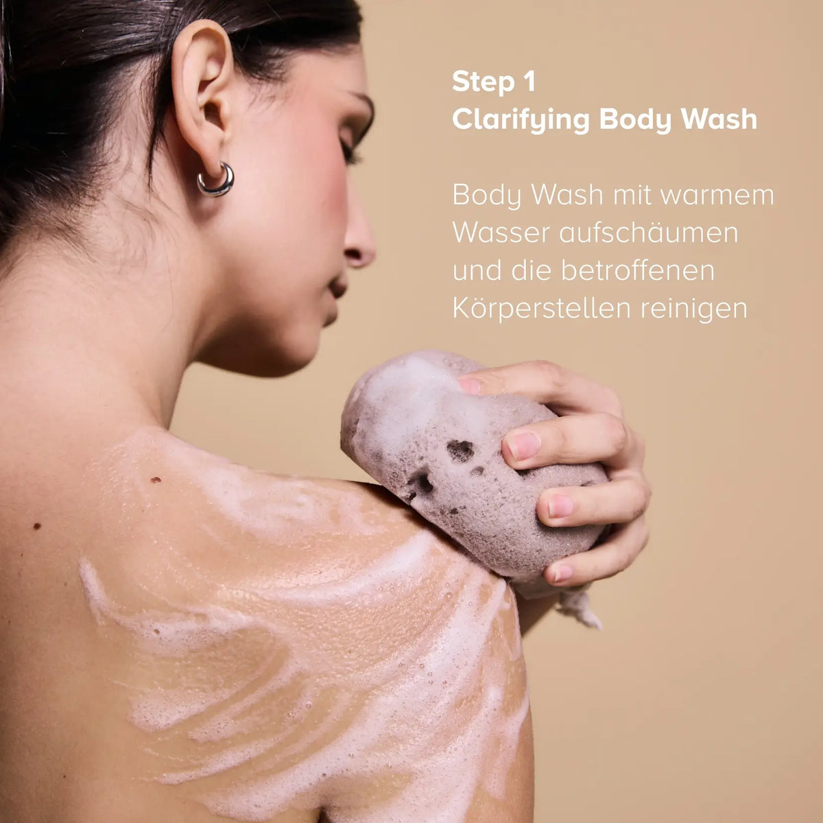 Step 1 des Clarifying Body Duo: Frau schäumt den Clarifying Body Wash mit einem Schwamm auf der Schulter auf