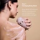 Step 1 des Clarifying Body Duo: Frau schäumt den Clarifying Body Wash mit einem Schwamm auf der Schulter auf