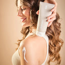 Frau mit Creme auf Schulter hält Tube mit Körpercreme.
