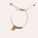 Das Charity Bracelet mit goldenen Perlen und Anhänger liegt auf hellem Hintergrund.